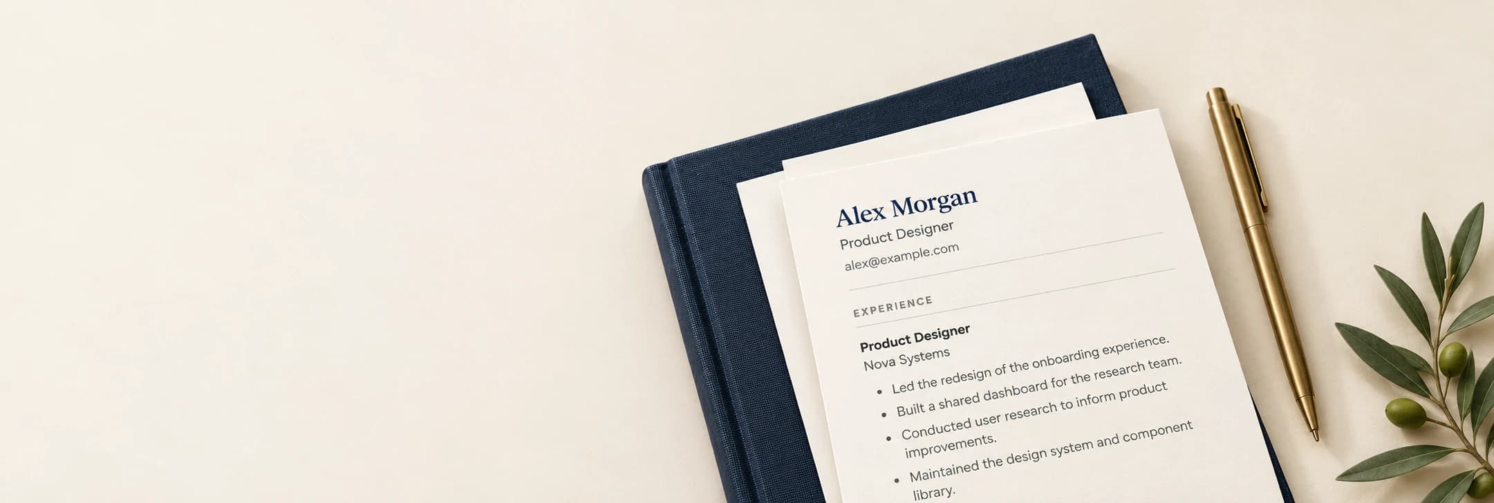 Illustrative résumé on layered cream paper and a navy notebook, with a brass pen and olive sprig